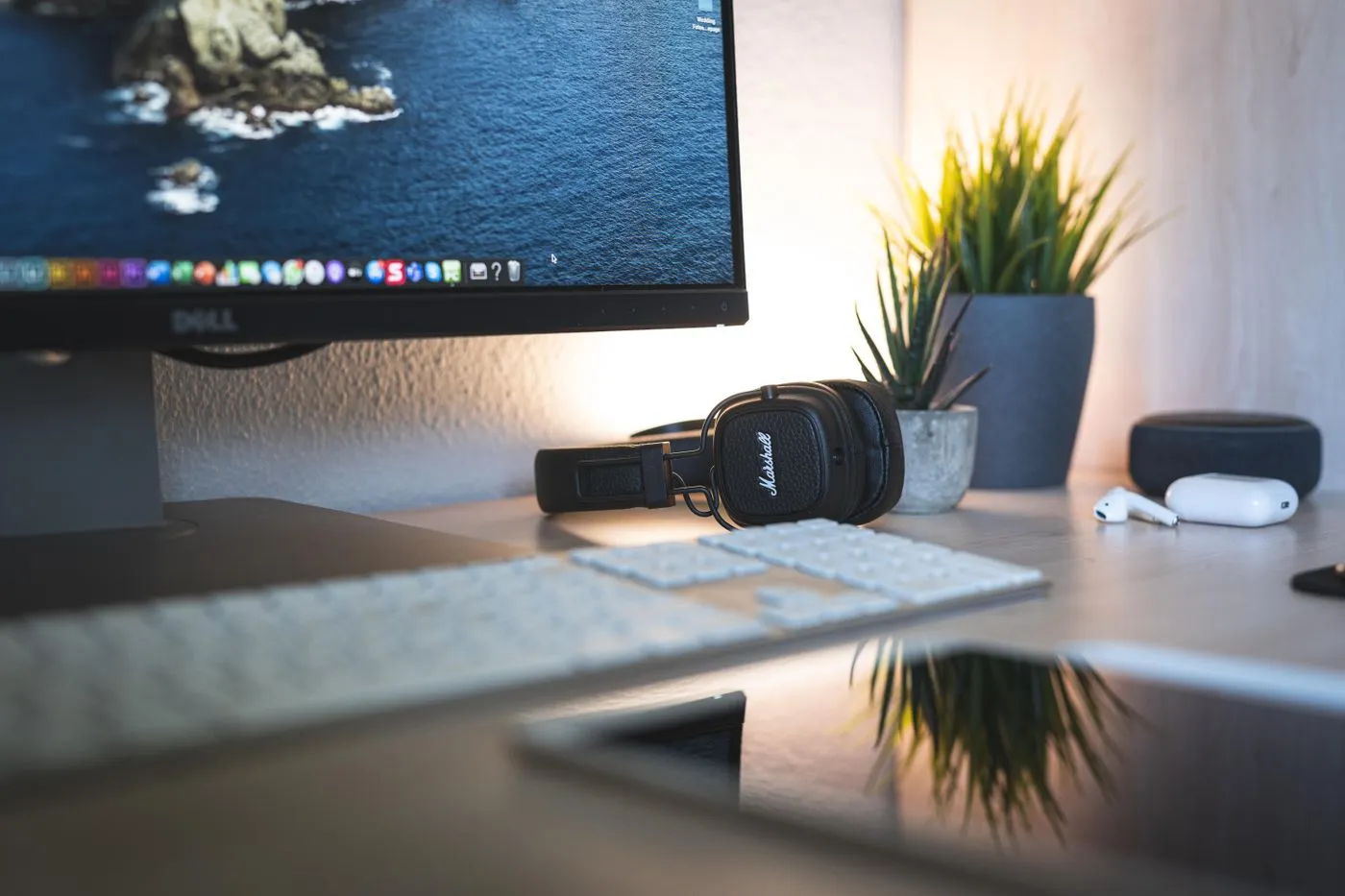 Desktop monitor, keyboard, and headphones on a desk beside plants